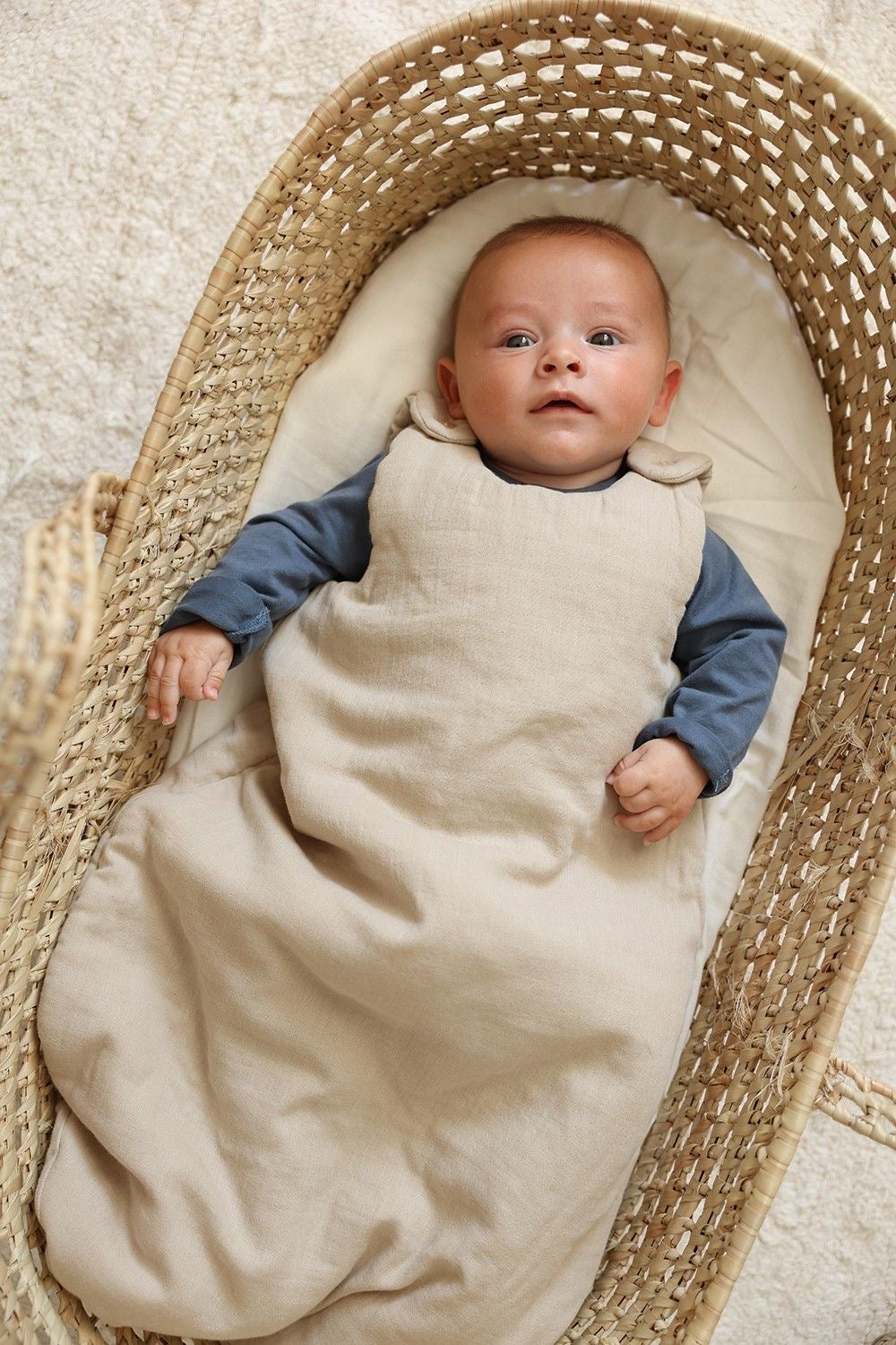 Un bébé est allongé dans un couffin, vêtu d'une gigoteuse beige 